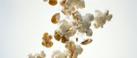 Popcorn kernels flying and falling through air against white background creating dynamic motion effect for snack food advertising and kitchen concepts.