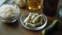 Dietary supplements and probiotics capsules with fermented foods like sauerkraut and pickled cucumber on wooden table, natural gut health concept.