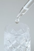 Clear glass dropper dispensing liquid into crystal cut glass container on light background, minimalist composition for cosmetic and wellness products.