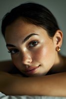 Young woman with natural makeup resting chin on arms looking at camera with soft lighting and freckled skin for beauty and wellness concepts.