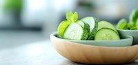 Fresh cucumber slices with mint leaves in wooden bowl on light background, healthy vegetable for salads and detox drinks.