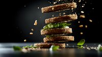 Levitating slices of dark rye bread with fresh green basil leaves and scattered crumbs against black background, dramatic food photography with motion effect.