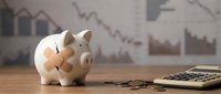 Pink piggy bank with coins and calculator on wooden desk against financial charts background showing investment savings and budget planning concepts.