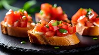 Fresh bruschetta appetizers with diced tomatoes, herbs and olive oil on toasted baguette slices, served on black slate plate in dramatic lighting.