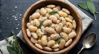 Cooked white beans with herbs and spices in wooden bowl on dark slate background. Healthy vegetarian protein source for Mediterranean cuisine recipes.