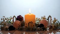 Autumn candle centerpiece with orange pillar candle, seasonal decorations, berries and warm lighting for cozy home decor and holiday celebrations.