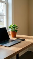 Laptop and smartphone on wooden desk with potted green plant by bright window, neutral beige wall background, modern workspace setup for remote work and productivity.