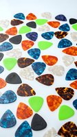 Colorful guitar picks collection scattered on white background featuring various patterns and colors for music accessories and instrument supplies.