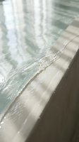 Clear turquoise pool water gently lapping against concrete edge with soft ripples and reflections creating peaceful aquatic atmosphere for relaxation concepts.