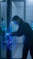 IT technician working in server room with blue lighting connecting network cables for data center maintenance and computer infrastructure support.