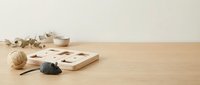 Wooden cat puzzle toy with rope ball and plush mouse on a light oak table with eucalyptus branch and ceramic bowl in background.