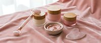 Luxury skincare cosmetics set with rose quartz facial roller and gua sha stone on pink silk fabric for spa beauty routine and self-care wellness treatment.