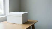 White cardboard storage box with lid on wooden table near window in minimalist room interior for organizing and decluttering home office space.