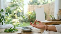 Woman with medium skin tone holding blank white card indoors near plants and natural window light, suitable for greeting cards, invitations, announcements, and marketing materials.
