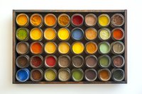 Colorful array of aromatic spices and seasonings in metal containers organized neatly in wooden box, top view showing vibrant yellows, reds, greens and browns.