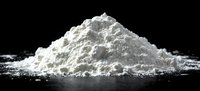 White powder pile on black reflective surface with scattered particles, dramatic studio lighting creates contrast between substance and dark background.
