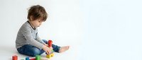 Young boy with brown hair sitting on floor playing with colorful building blocks and toys, isolated on white background for design projects.