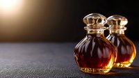 Elegant glass perfume bottles with golden caps containing amber and red fragrances on textured surface with warm lighting for luxury cosmetics branding.