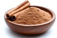 Ground cinnamon powder in wooden bowl with whole aromatic spice sticks, close up view on white background, for cooking and baking designs.