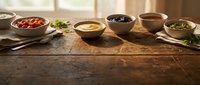 Rustic wooden table with various colorful spices and seasonings in ceramic bowls, warm natural lighting creates cozy kitchen atmosphere for cooking.
