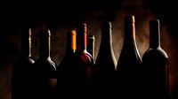 Silhouettes of wine bottles arranged in a row against dark background, creating dramatic lighting effect for wine cellar or restaurant ambiance.