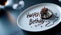 Elegant chocolate dessert with Happy Birthday message written on white plate against dark moody background, selective focus creates intimate celebratory atmosphere.