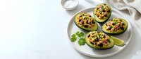 Stuffed avocado halves topped with corn, black beans, and cheese served on white plate with lime wedges and cilantro garnish for healthy meal preparation.