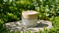 Frosted glass cosmetic jar with wooden lid on stone surface surrounded by lush green plants in natural sunlight.