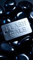 Metal tag engraved with Flash Sale text resting on shiny black stones, dark moody background for retail promotion and marketing campaigns.
