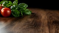Fresh red tomatoes and green basil leaves on rustic wooden table with dark background, dramatic food photography composition with copy space.
