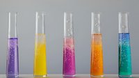 Colorful chemical reactions in glass test tubes showing vibrant purple, yellow, pink, orange, and turquoise liquids with bubbling effervescence on gray background.