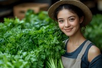 Young woman with dark hair and olive complexion wearing straw hat and apron harvesting fresh parsley in organic garden for agriculture and farming concepts.