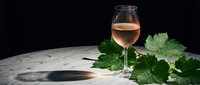Elegant rosé wine glass with fresh grape leaves on marble surface against dark background for luxury dining and winery marketing materials.