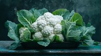 Fresh organic cauliflower with green leaves on dark rustic wooden background. Natural light food photography for healthy eating and vegetarian cuisine.