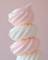 Stack of pastel pink and white swirled meringue cookies on soft pink background for dessert and confectionery designs.