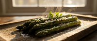 Fresh grilled asparagus spears with herbs on rustic wooden cutting board in warm kitchen sunlight for healthy cooking and gourmet dining concepts.