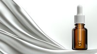 Amber glass dropper bottle with elegant white silk fabric flowing in background on white surface, minimalist cosmetic product presentation for skincare.