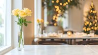 Yellow roses in glass vase on windowsill with festive Christmas dinner table and golden lights creating warm holiday home atmosphere for celebrations.