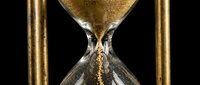 Hourglass with golden sand flowing through narrow center against black background, symbolizing passage of time and deadline concepts for business and productivity themes.