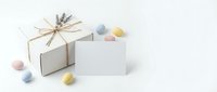 White gift box with natural twine bow and blank card surrounded by colorful Easter eggs on clean background for spring holiday celebrations.
