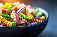 Colorful pasta salad with spiral noodles, fresh herbs, red onion and meat in dark bowl. Healthy Mediterranean cuisine for lunch or dinner preparation.