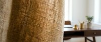 Natural burlap fabric texture close-up with blurred home interior background showcasing organic textile weave pattern for rustic decor projects.