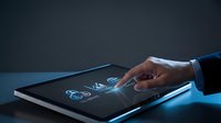 Hand touching digital tablet screen displaying holographic icons and data visualization in dark studio setting with blue lighting.