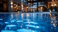 Floating candles creating magical atmosphere in blue pool water with blurred luxury interior background. Romantic evening spa setting.