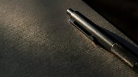Sleek metallic tactical pen resting on dark textured surface, dramatic moody lighting highlighting premium craftsmanship and minimalist design.