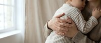 Tender moment as a parent gently holds a sleeping infant in a cozy home setting, capturing love, care, and family bonding.