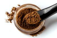 Ground coffee powder in glass jar with black measuring spoon, scattered aromatic coffee grounds on white background, macro food photography.