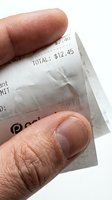 Close-up of human hand holding crumpled receipt showing total amount, isolated on white background for finance and expense tracking concepts.