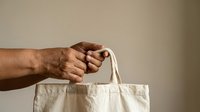 Male hand holding natural cotton tote bag against neutral background. Eco-friendly shopping and sustainable lifestyle concept for retail and environmental campaigns.