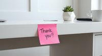 Pink sticky note with thank you message on white desk in modern office workspace for gratitude and appreciation concepts.